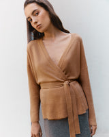 Woman posing in a wrap-style top against a plain background.