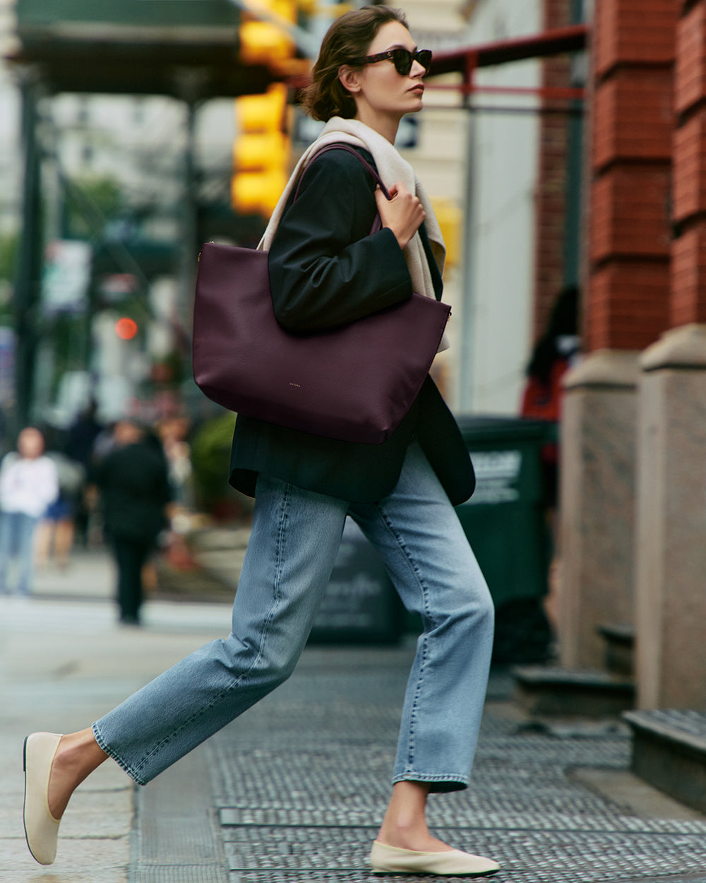 Person walking on sidewalk carrying large bag, wearing casual clothes and sunglasses.