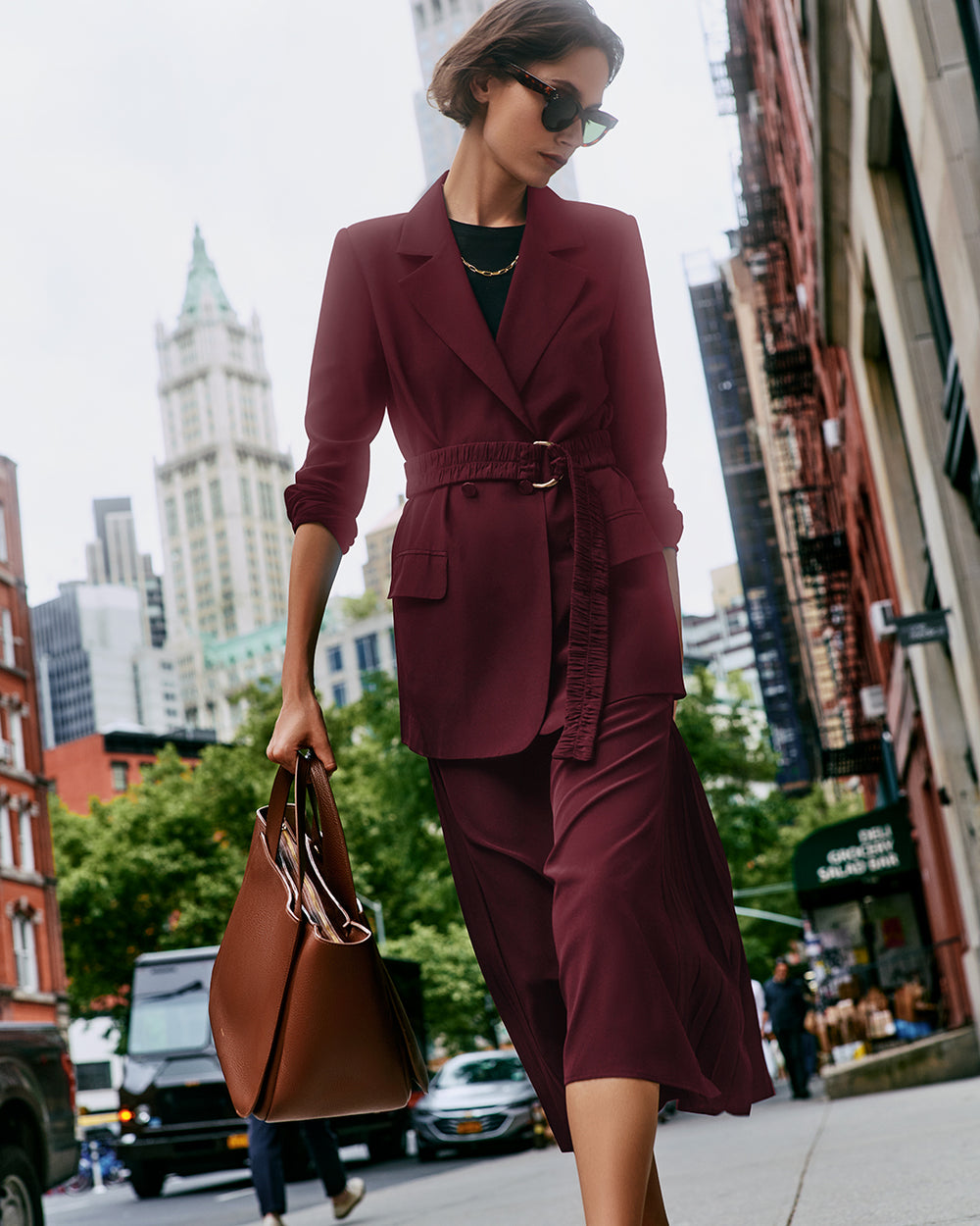 Person in a red blazer and skirt walking on a city street, carrying a large handbag