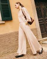 Person in matching top and wide-leg pants walking with shoulder bag near a building.