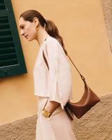 Woman with shoulder bag facing sideways against textured wall and window.