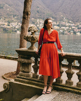 Woman in a dress standing by a railing overlooking a lake and hills.
