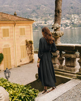 Person standing by a stone railing overlooking a scenic view of a lake and hillside houses.