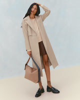 Model wearing long coat, top, pleated skirt, holding a large shoulder bag