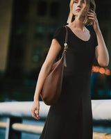 Person in dress holding a bag over shoulder standing outdoors.