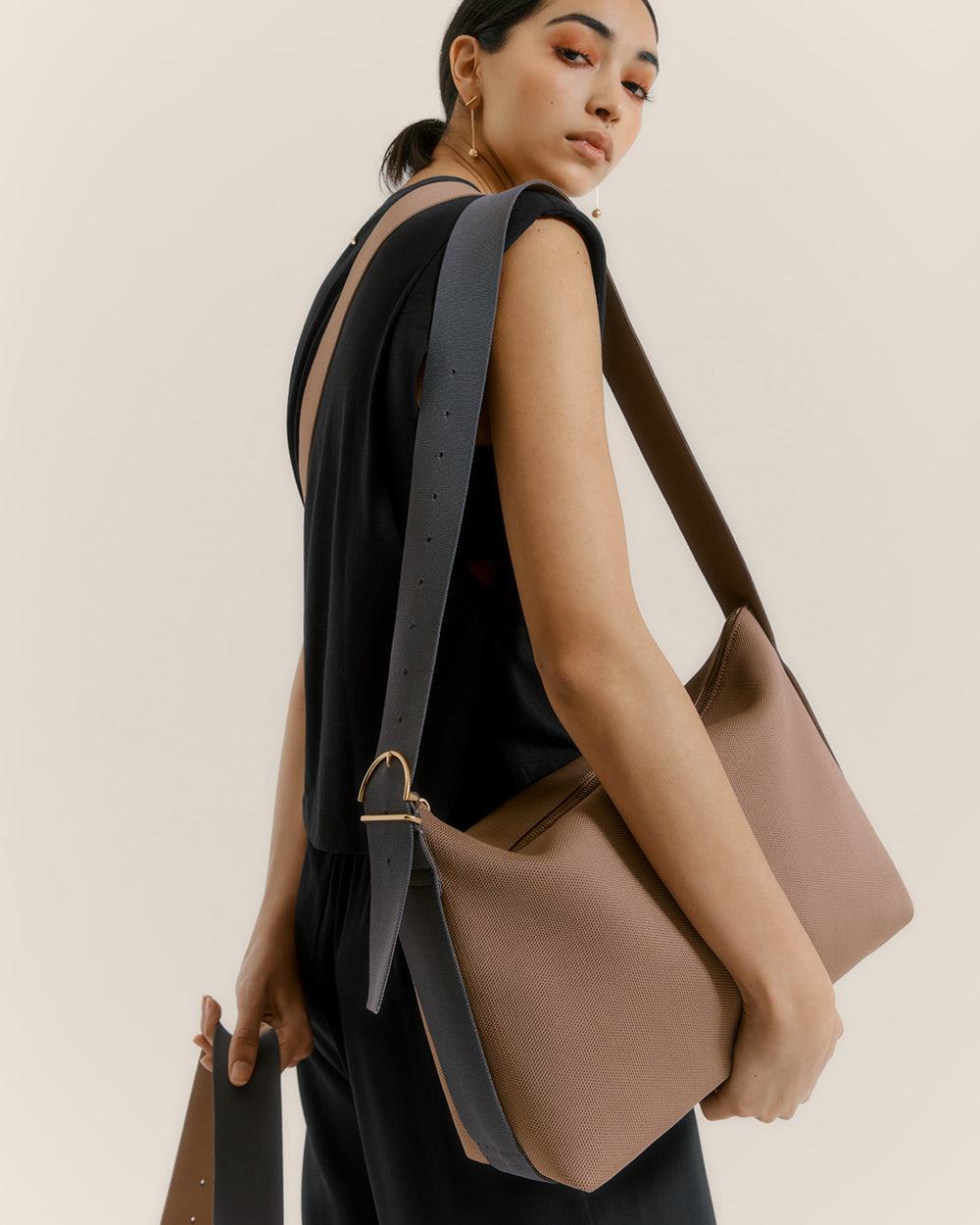 Person carrying a large shoulder bag over their left shoulder, looking back over their right shoulder
