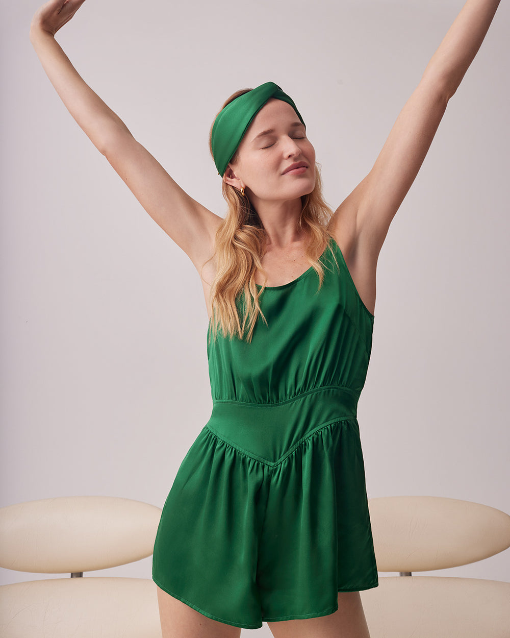 Woman stretching arms in a romper and headband, standing indoors.