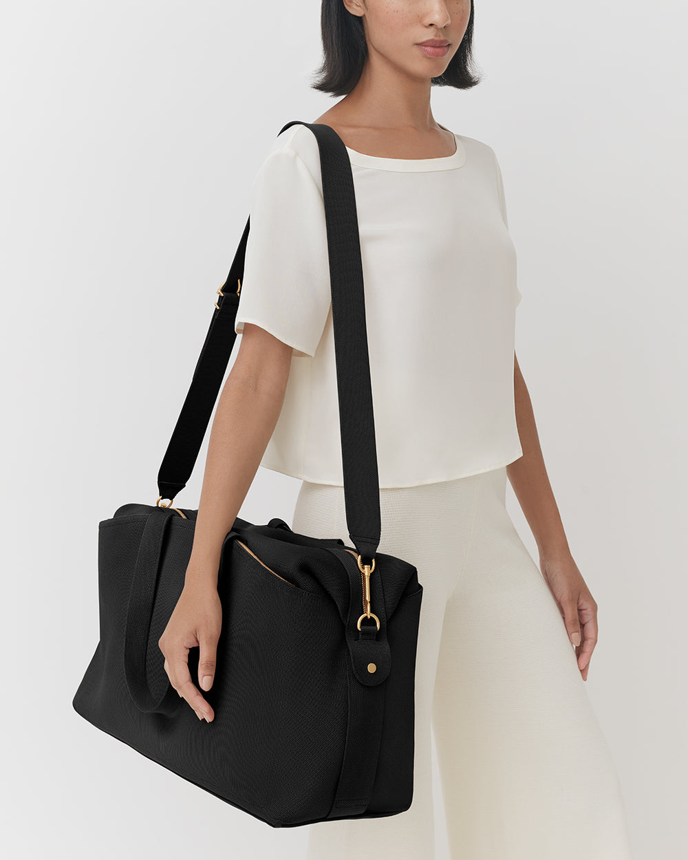 Person holding a travel bag wearing a top and pants.