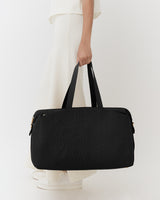 Person holding a travel bag standing against a plain background.