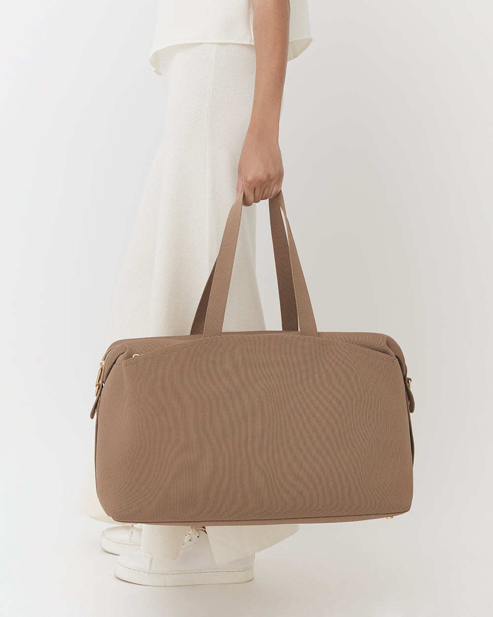 Person holding travel bag wearing skirt and sneakers.