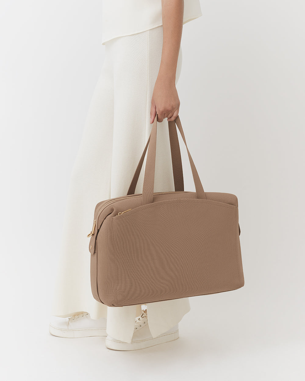 Person holding a travel bag, wearing long pants and shoes.