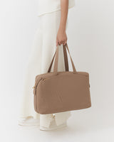 Person holding a travel bag, wearing long pants and shoes.