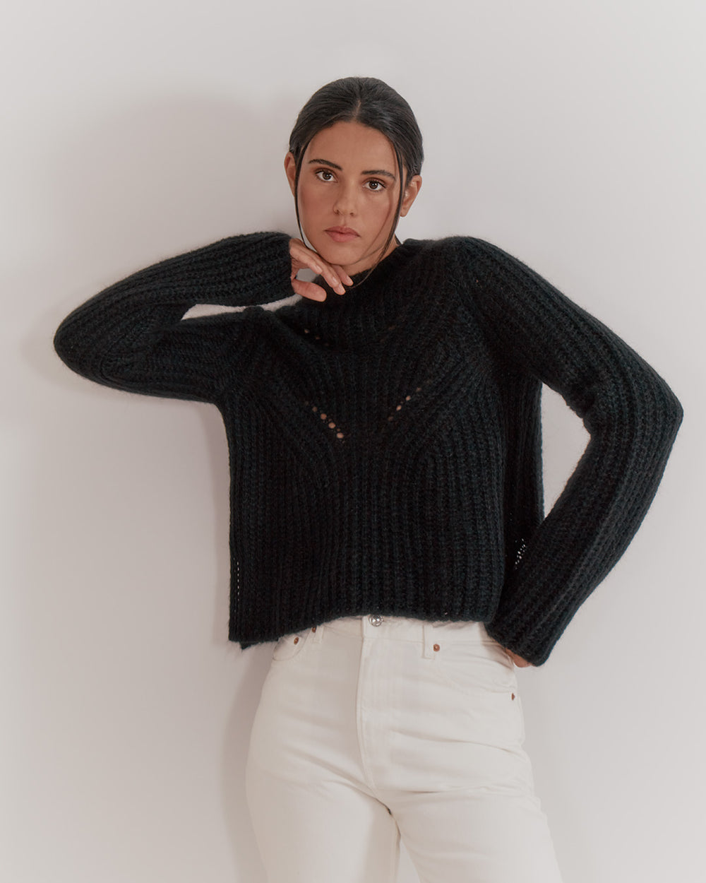 Woman standing with one hand on her hip, other touching her face.