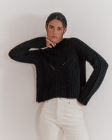 Woman standing with one hand on her hip, other touching her face.