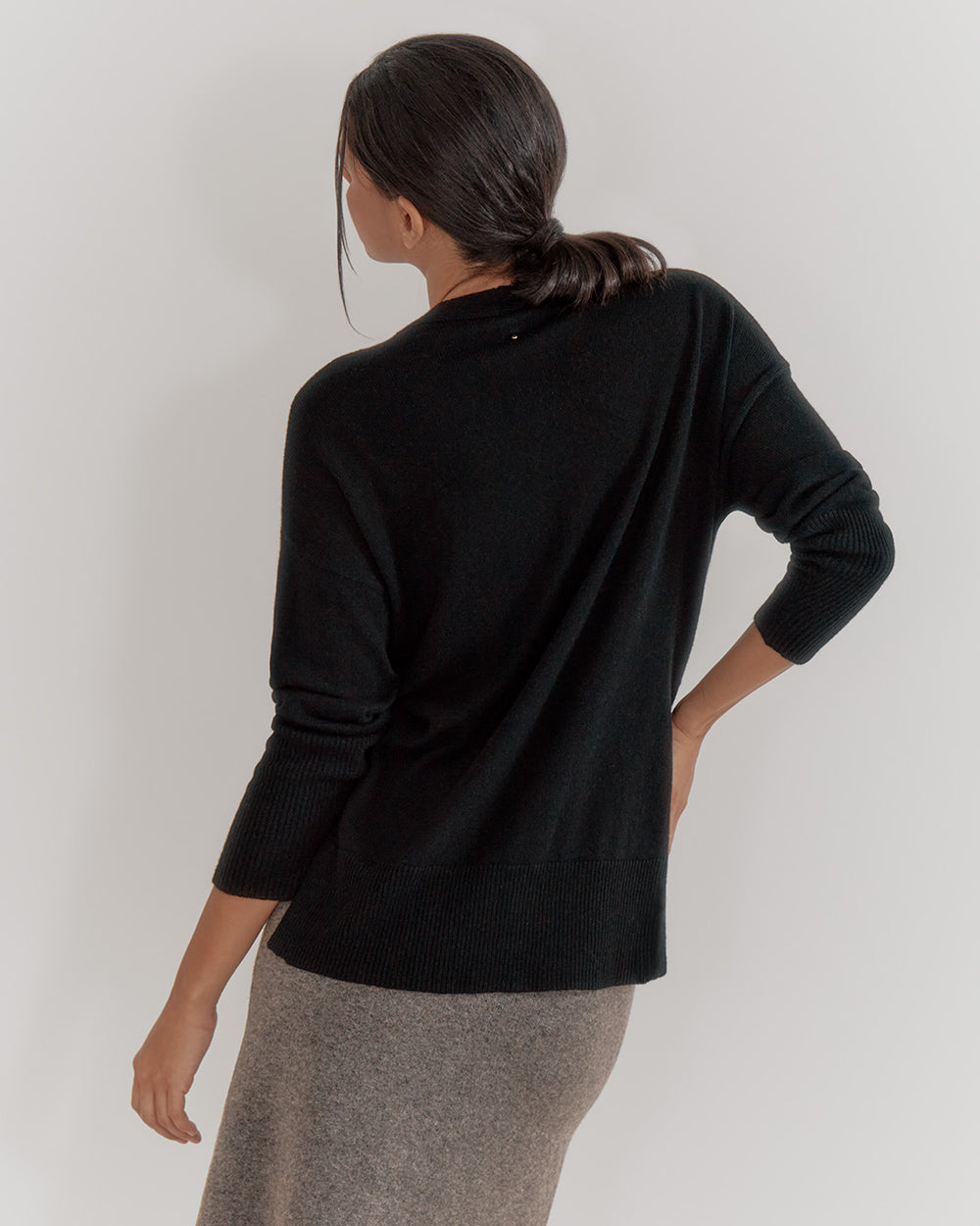 Woman facing away from the camera, wearing a sweater and skirt.