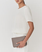 Person holding a clutch bag while wearing a short-sleeved top.