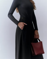 Person wearing long-sleeve top and pants, holding a small handbag.