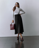 Person wearing a fitted top and long skirt, holding a tote bag and wearing sunglasses.