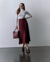 Person wearing a fitted top and long skirt, holding a tote bag and wearing sunglasses.