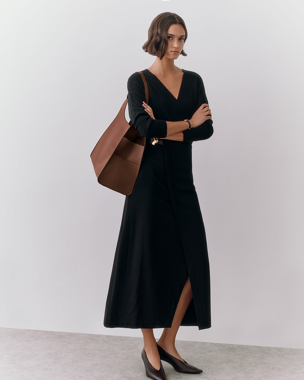 Person in a long dress holding a large shoulder bag, standing indoors.