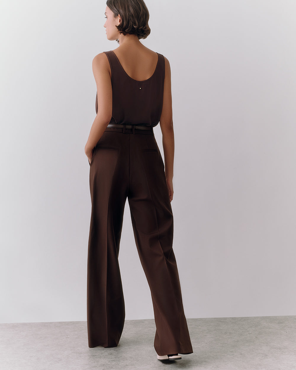 Person in a sleeveless top and wide-leg pants standing against a plain backdrop.