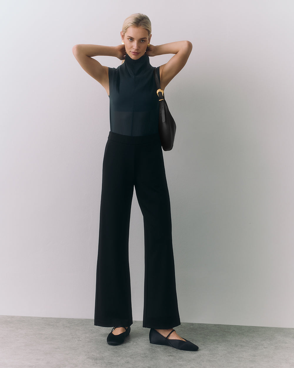Person posing in sleeveless top and wide-leg pants, holding bag on shoulder