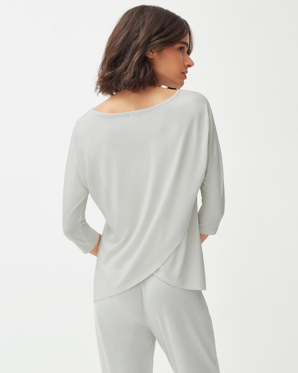 Woman standing, seen from behind, wearing a long sleeve top and pants.