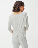 Woman standing, seen from behind, wearing a long sleeve top and pants.