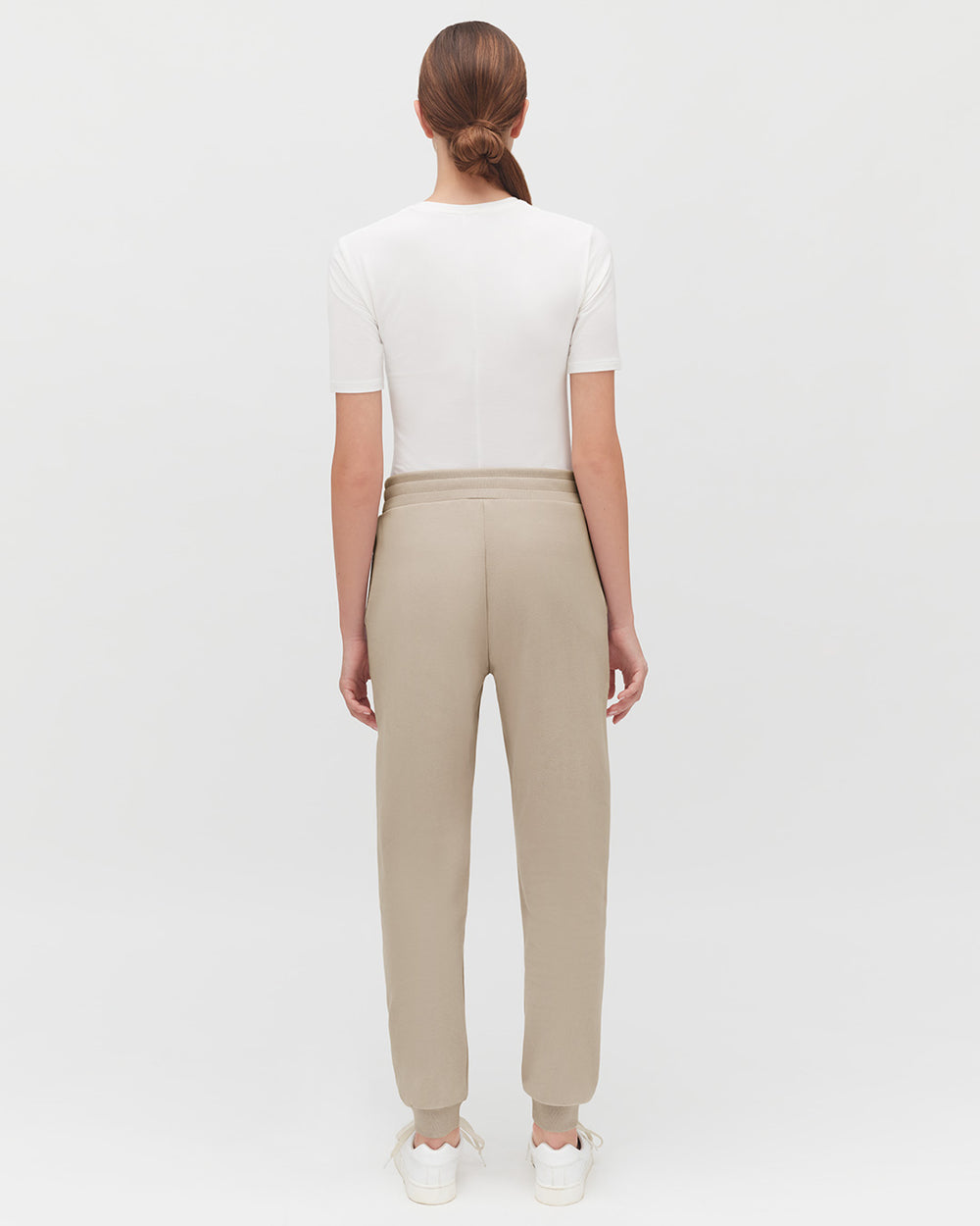 Woman standing with her back to the camera, wearing a top and pants.