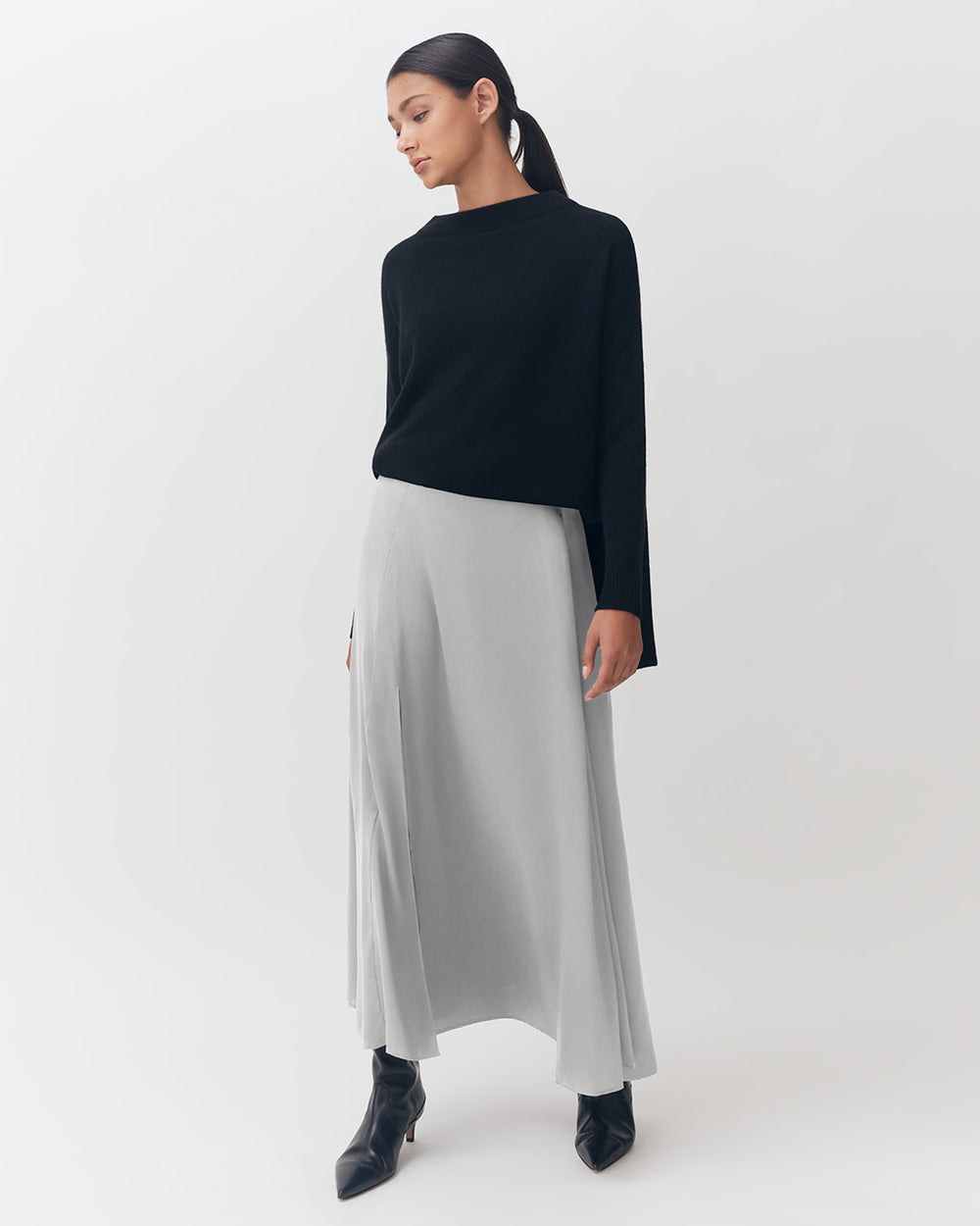 Woman standing in a studio wearing a long skirt and top with boots.