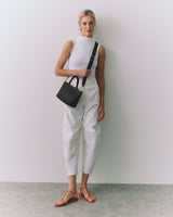 Person standing with a handbag, wearing sleeveless top and pants, sandals on feet.