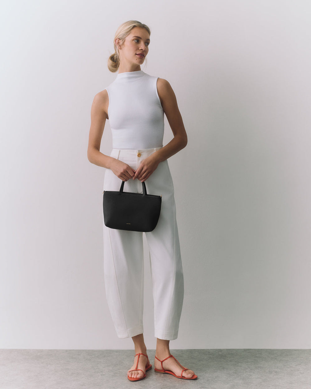 Person posing with a handbag, wearing sleeveless top and trousers.