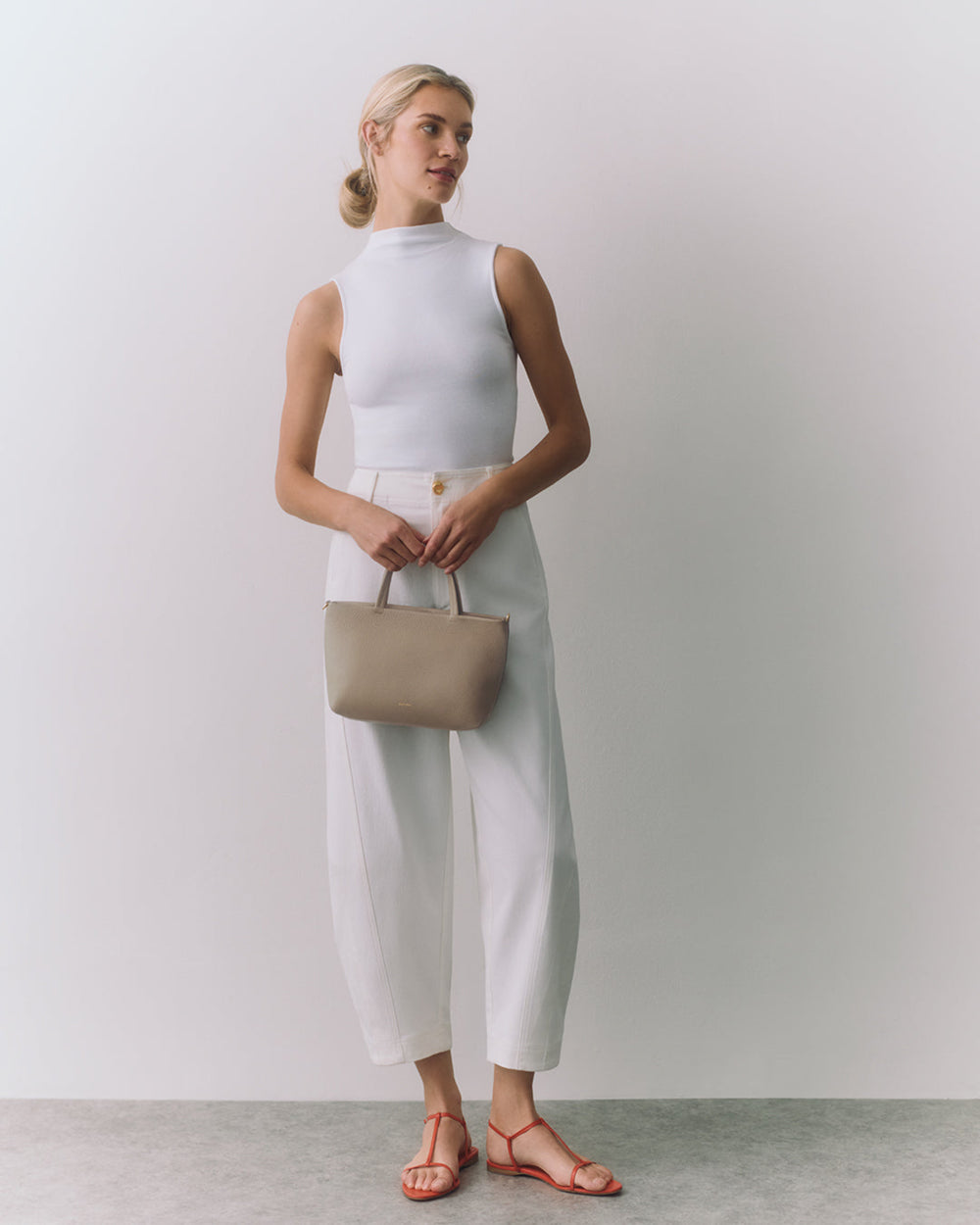 Person wearing sleeveless top and wide pants holds handbag, standing in sandals.