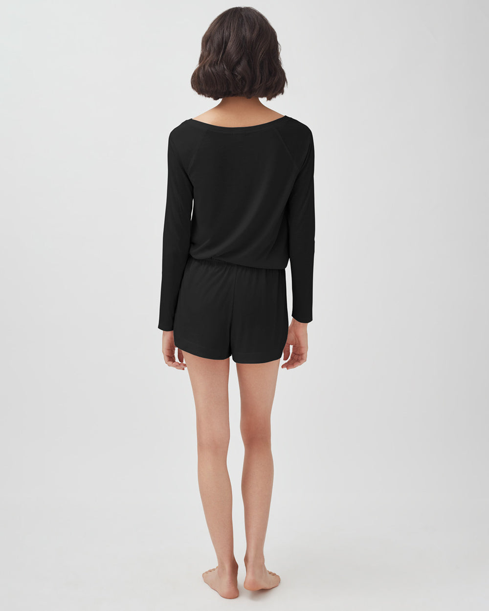 Woman standing with her back to the camera wearing a long-sleeve top and shorts.