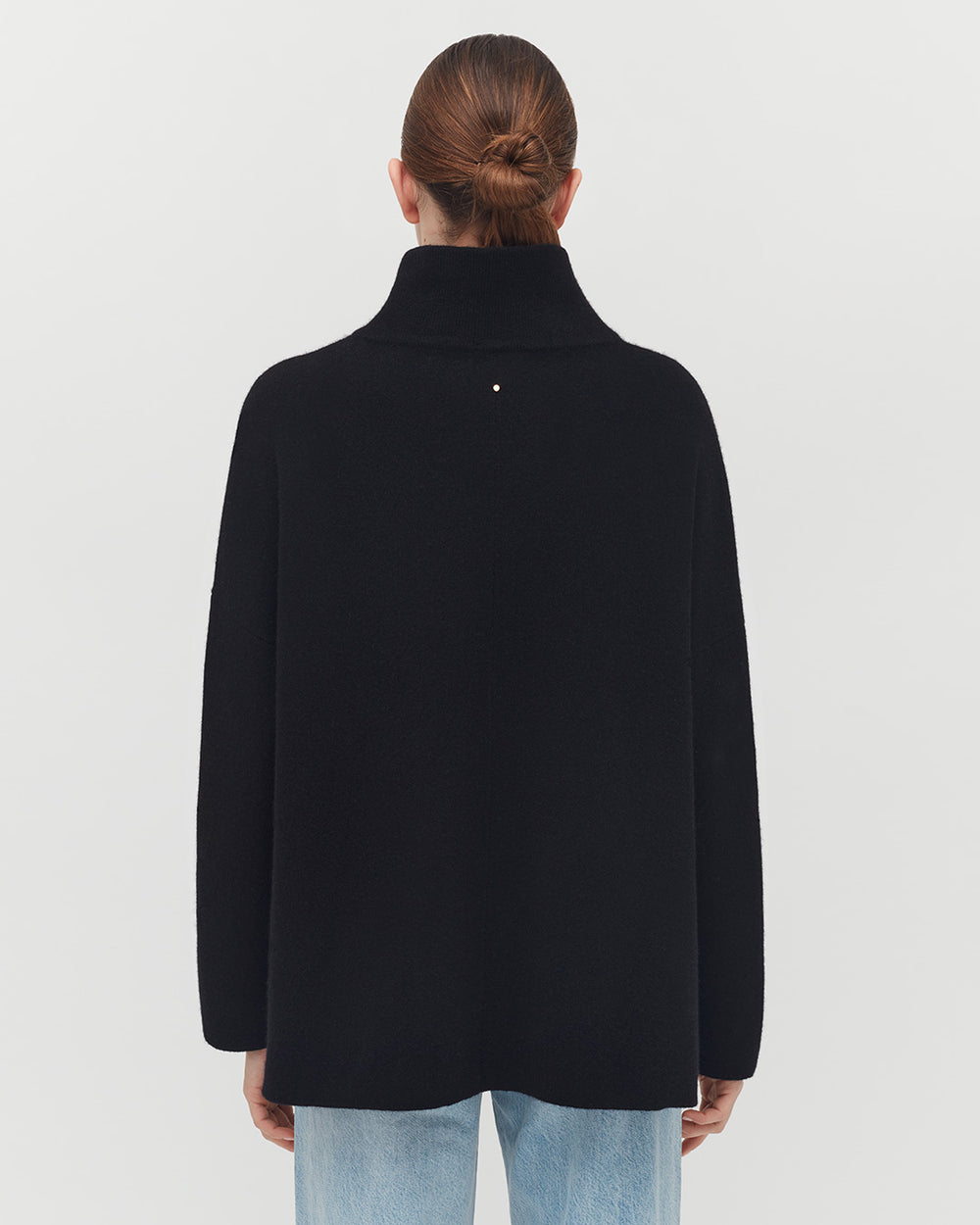 Woman wearing a turtleneck and jeans, viewed from behind with hair up.