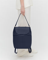 Person holding a handbag, standing against a plain background.
