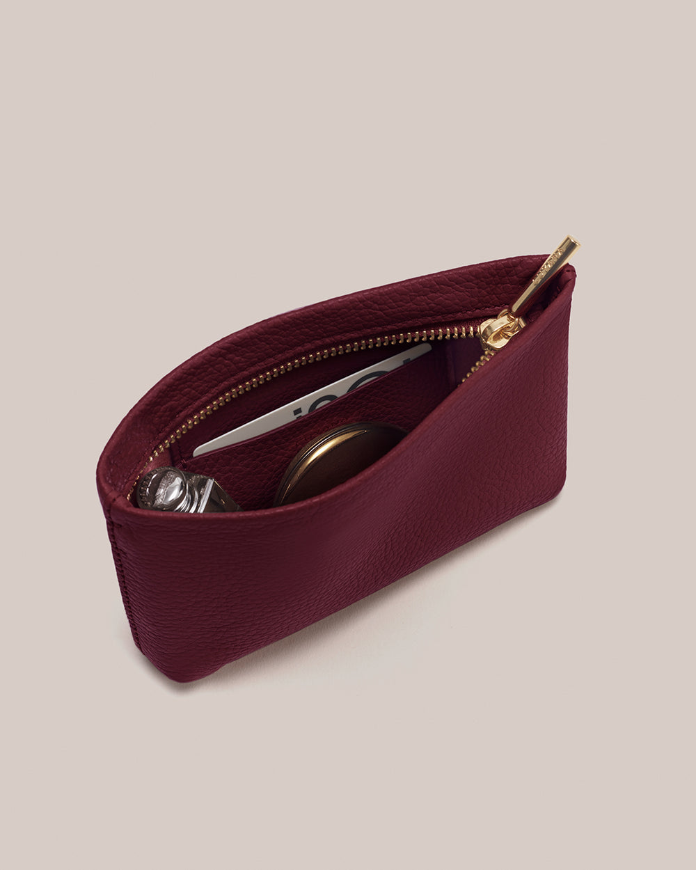 Open pouch with zipper, containing a card, perfume and a compact mirror.
