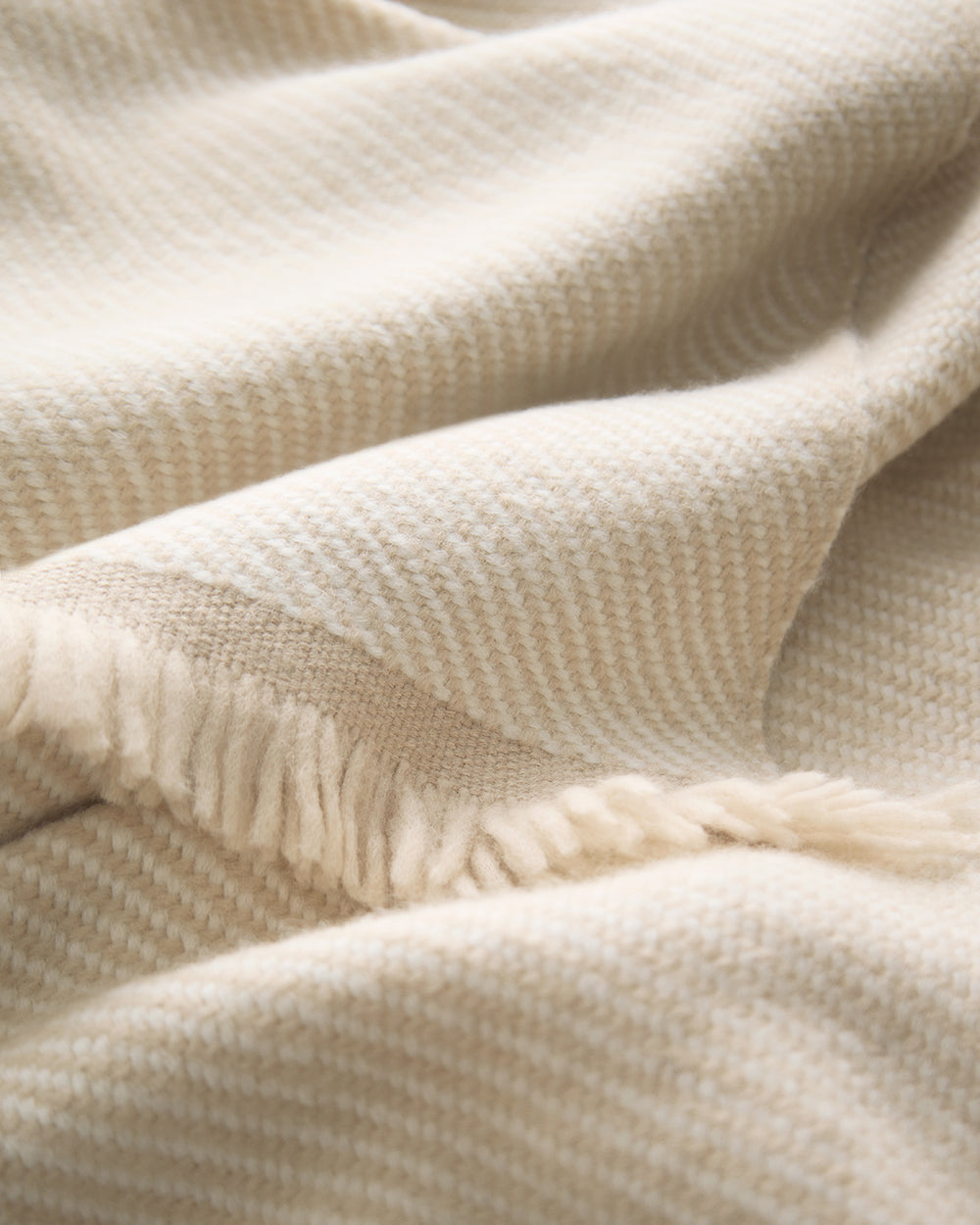 Close-up of a folded blanket with fringe edges in a soft, textured pattern.