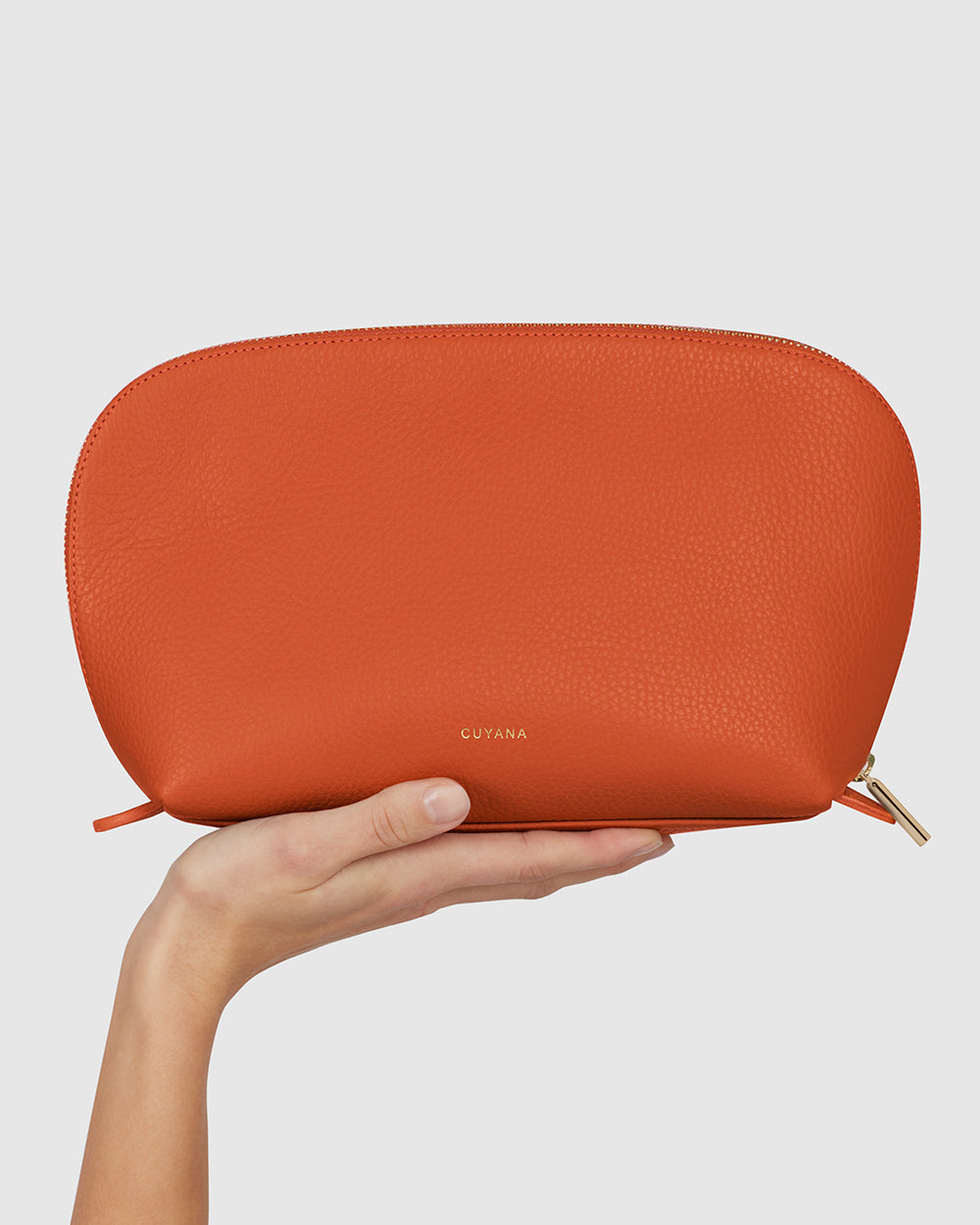 Hand holding a textured zippered pouch with brand name.