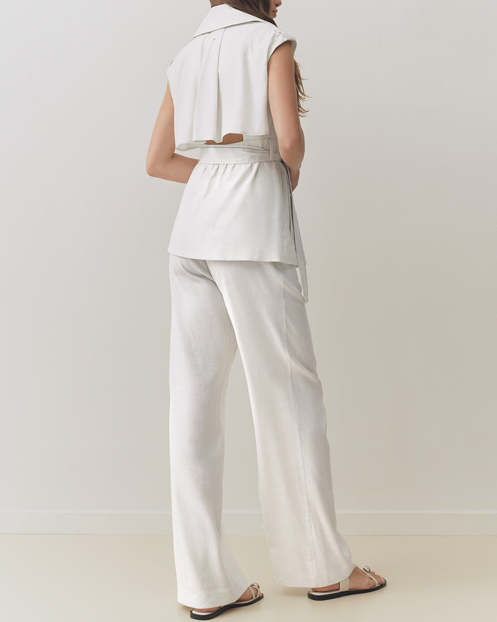 Woman standing, viewed from the back, wearing a sleeveless top and pants.