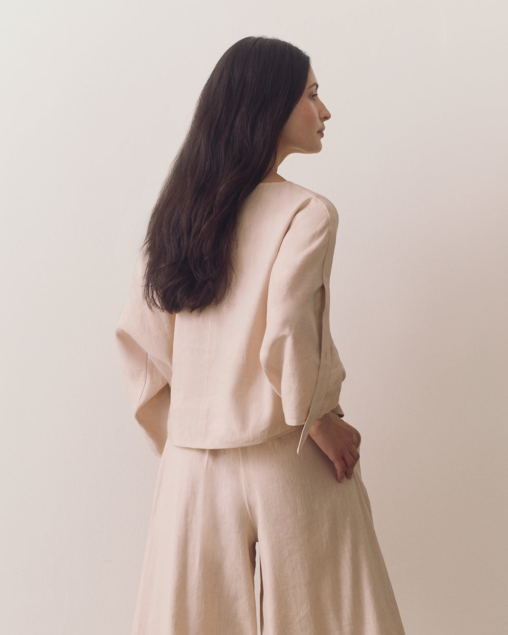 Person wearing loose top and wide-leg pants standing against plain backdrop