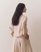 Person wearing loose top and wide-leg pants standing against plain backdrop
