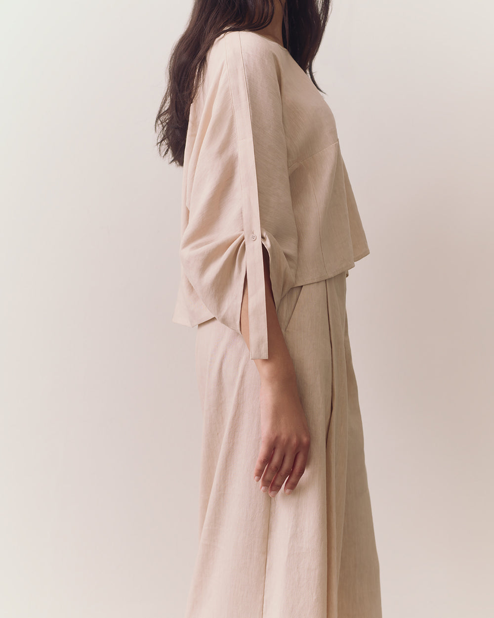 Person wearing loose top and wide-leg pants standing against plain backdrop