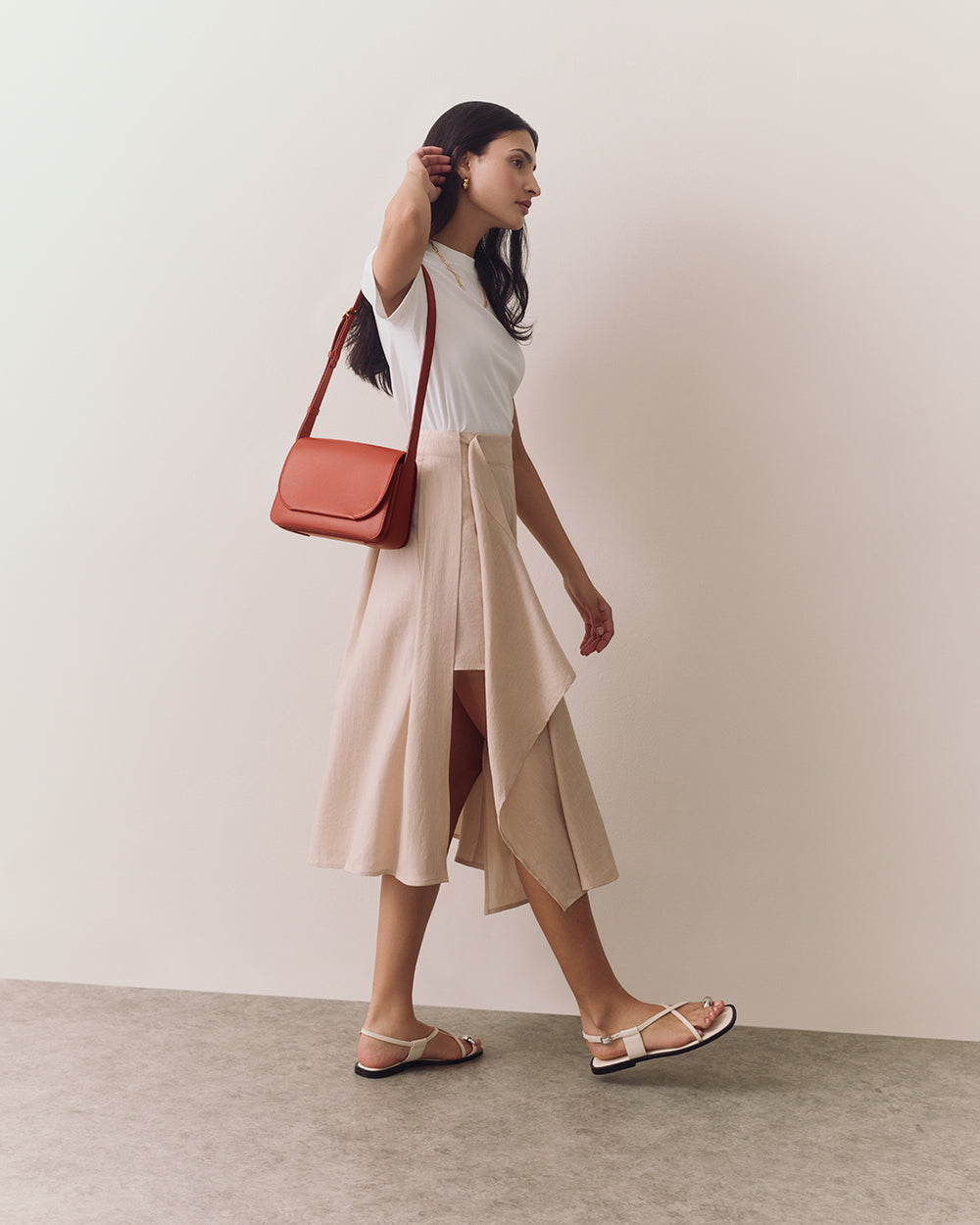 Person walking with shoulder bag and wearing sandals and a skirt.