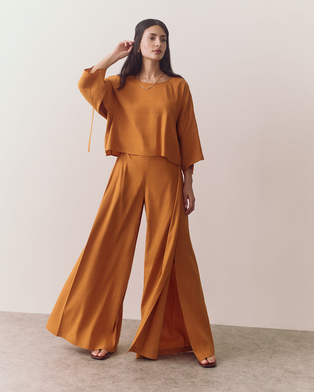 Person wearing a long-sleeve top and wide-leg pants, standing on a plain background.