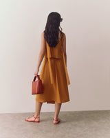 Person in a sleeveless top and flowy skirt, holding a bag, wearing sunglasses and sandals, facing away from the camera.