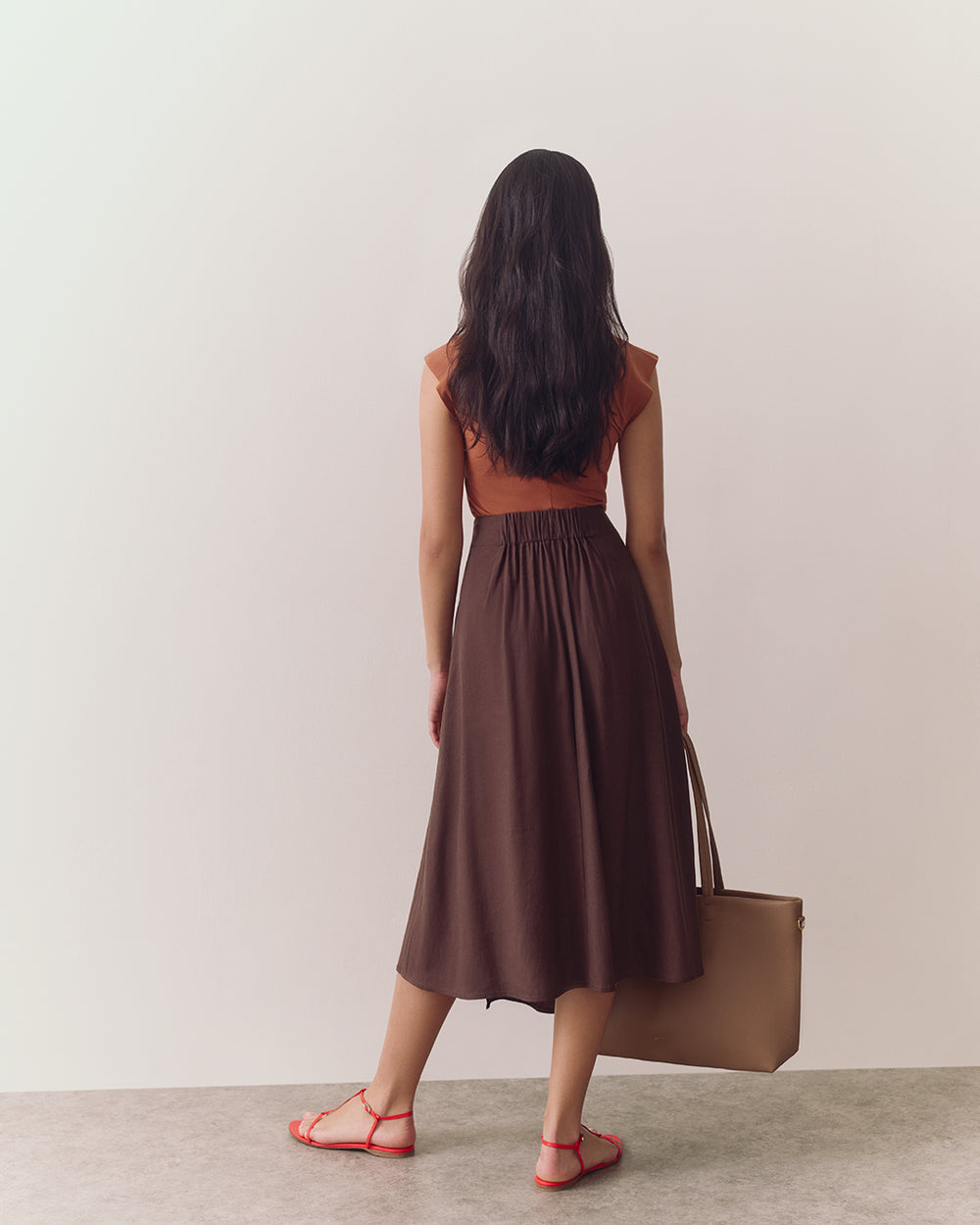 Person wearing a T-shirt and skirt, facing away, standing on a plain floor.