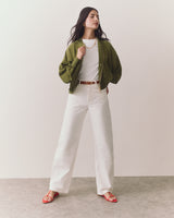 Person wearing open jacket, t-shirt, wide pants, sandals, and necklace standing confidently
