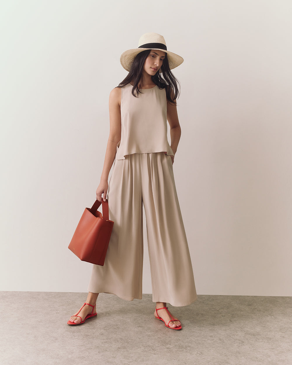 Person wearing a sleeveless top, wide-leg pants, hat, sandals, holding a bag.