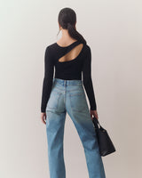 Person facing away, wearing open-back top and jeans, holding handbag.